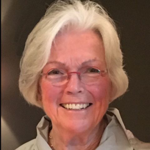 A woman with short graying hair smiles warmly in a beige blouse