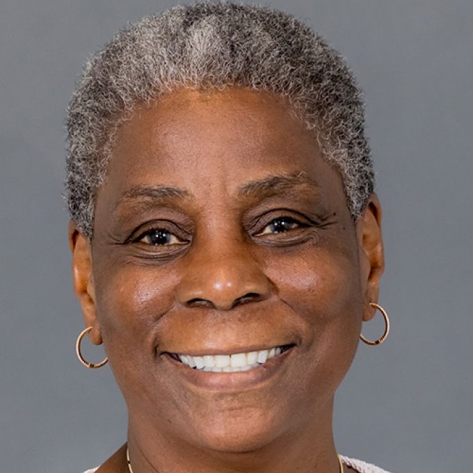A woman with very short salt and pepper hair smiles in front of a gray studio backdrop