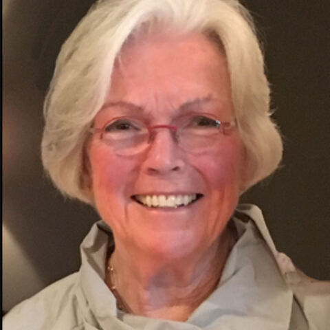 A woman with short graying hair smiles warmly in a beige blouse