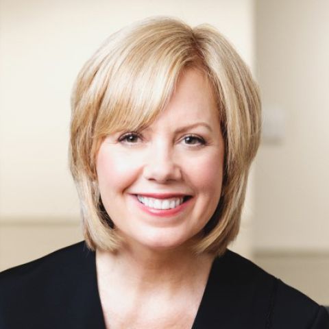 A woman with shoulder-length blonde hair smiles broadly in a black blouse