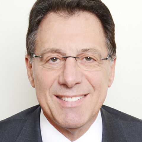 A man with neat brown hair poses in rimless eyeglasses wearing a dress jacket, white white, and light blue tie