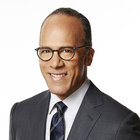 A balding man with trendy glasses poses in front of a white background in dark gray jacket, dress shirt, and navy tie with light gray stripes.