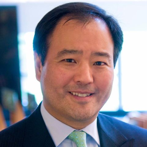 A man with short black hair smiles in a navy blazer, light dress shirt, and light green tie