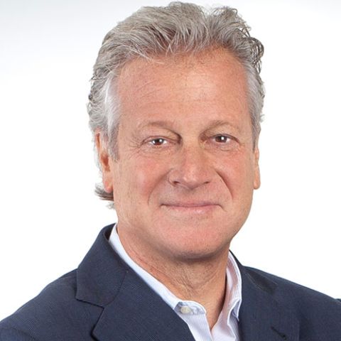 A man with neat, graying hair smiles in a navy blazer and light dress shirt