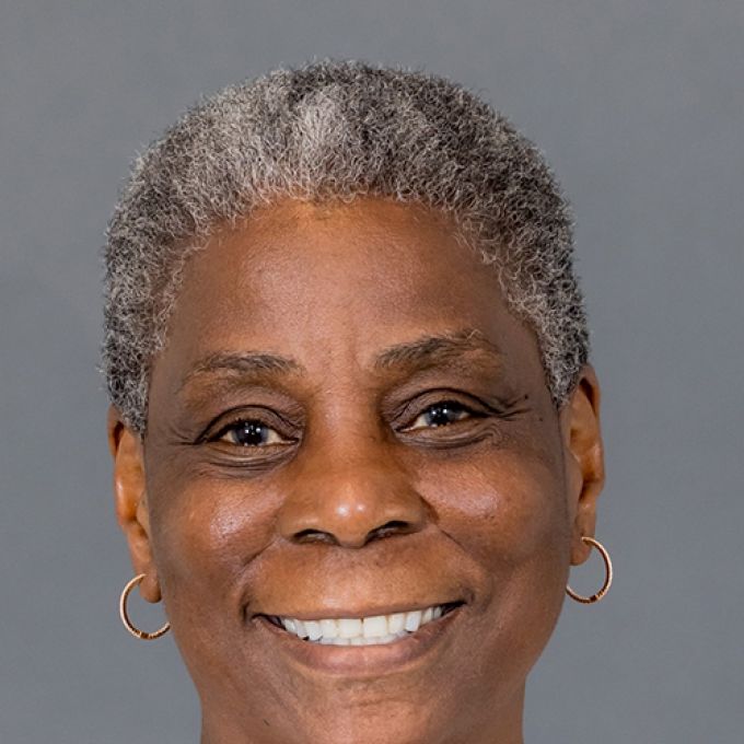 A woman with very short salt and pepper hair smiles in front of a gray studio backdrop