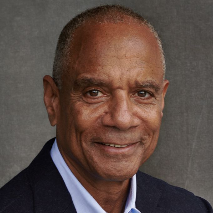 A man poses in front of a gray studio backdrop in black jacket and light blue dress shirt