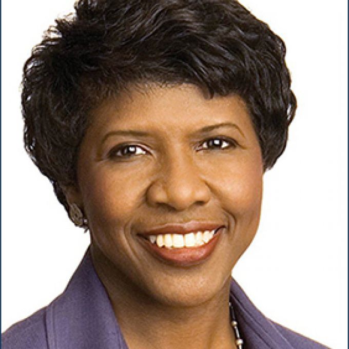 A woman with black hair smiles warmly in a purple blouse with a sliver necklace