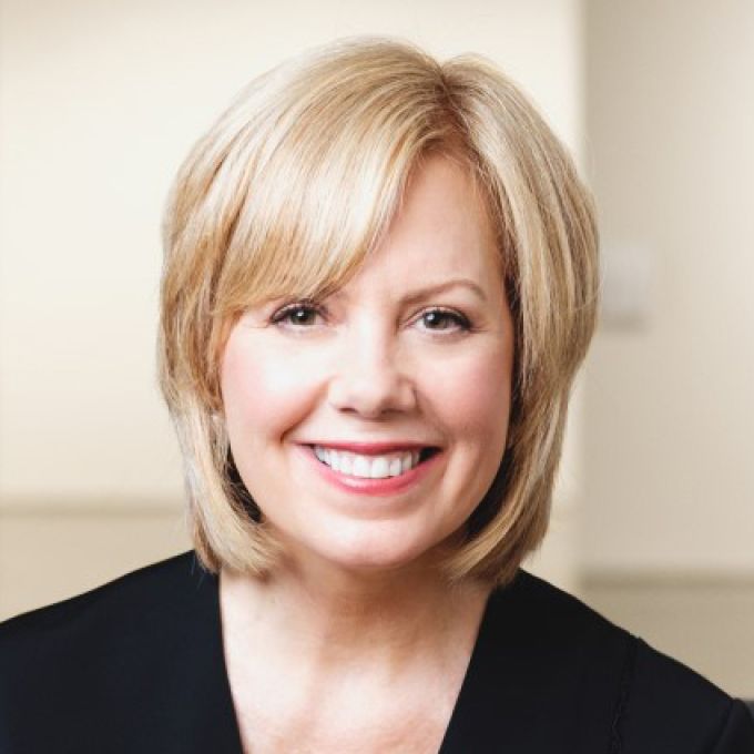 A woman with shoulder-length blonde hair smiles broadly in a black blouse