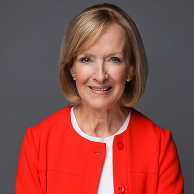 A woman with shoulder-length blonde hair poses with her arms crossed in a bright red jacket and white blouse