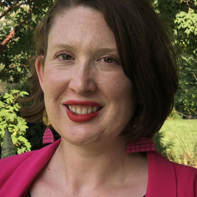 A woman with shoulder length brown hair poses outdoors in a pink jacket