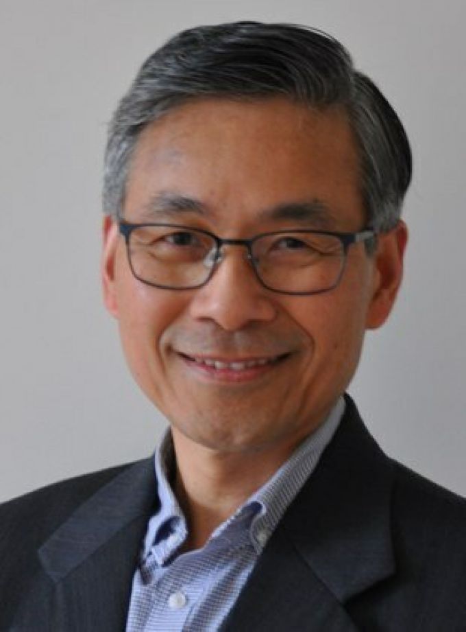 Man with neatly-trimmed graying hair smiles in a gray jacket and blue button down shirt.